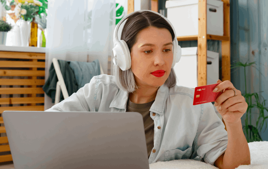 Frau mit Kopfhörern sitzt mit ihrem Laptop und ihrer Kreditkarte
